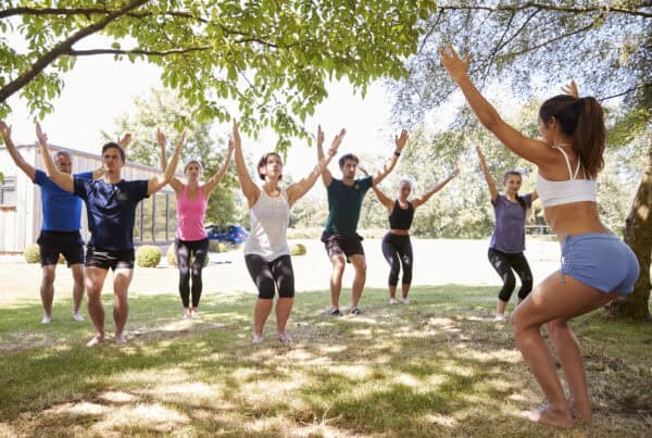 Female Instructor Leading Outdoor Yoga Class; Benefits of Exercise in Recovery