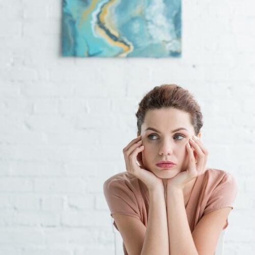 thoughtful young woman sitting at table in front of white brick wall with picture