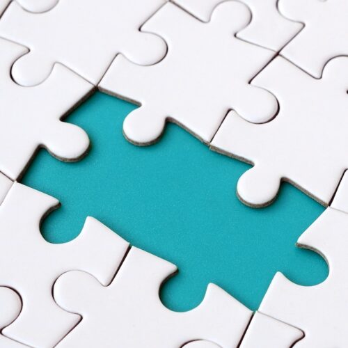 Close-up texture of a white jigsaw puzzle in assembled state with missing elements forming a blue pad for text.