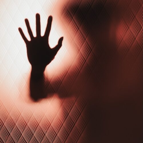 Behind knurled glass door a leaning persons hand asks for help