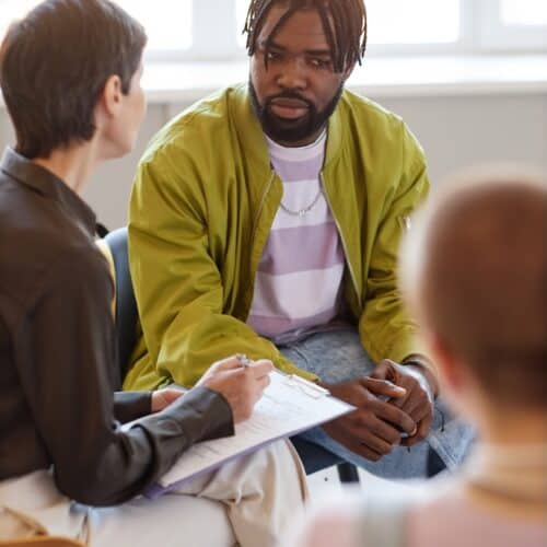 Vertical image of group of people talking to psychologist at session in the room