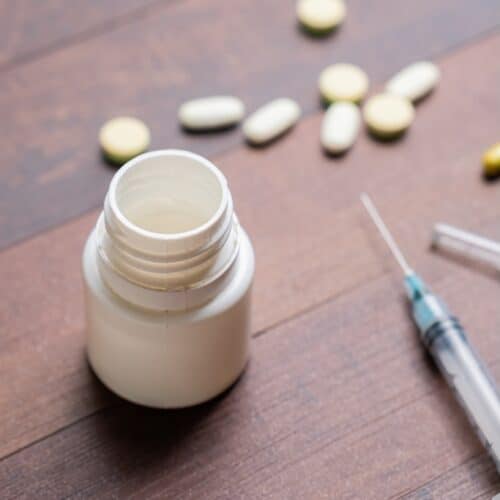 A wooden table with scattered pills, a syringe, and an open pill bottle