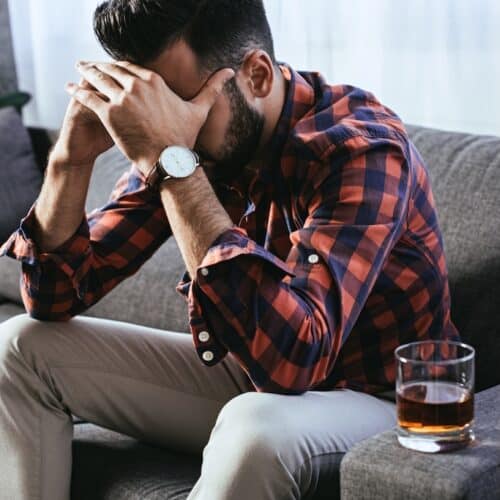 depressed young man with glass of whiskey sitting on couch